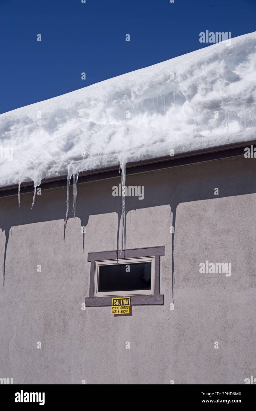 building wall and roof with snow and icicles and caution sign by window Stock Photo