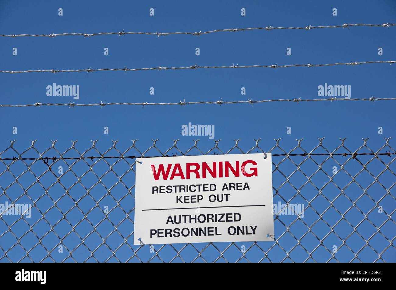 warning restricted area keep out authorized personnel only sign on a barbed wire chain link fence with blue sky background Stock Photo