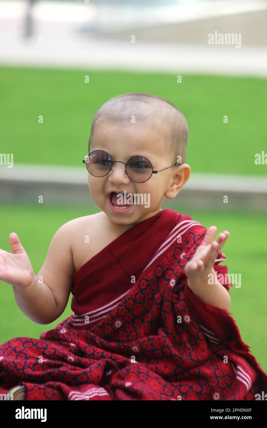a cute bald baby boy is dressed up in Monk avatar, wearing a maroon shawl, sun glass and giving a cute smile Stock Photo