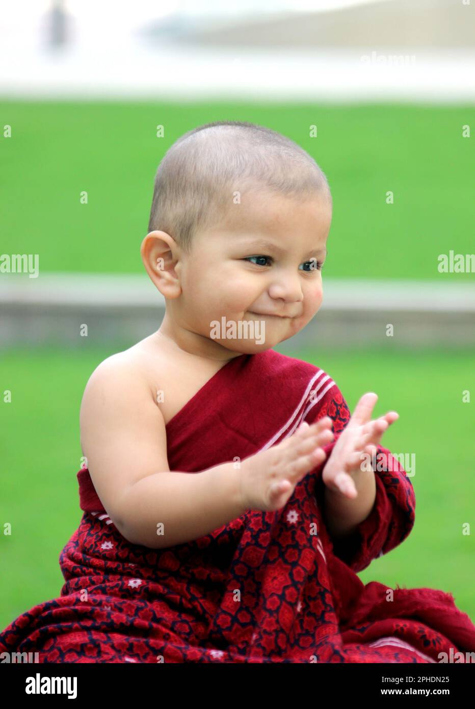 a cute bald baby boy is dressed up in Monk avatar, wearing a maroon shawl, and giving a cute smile Stock Photo