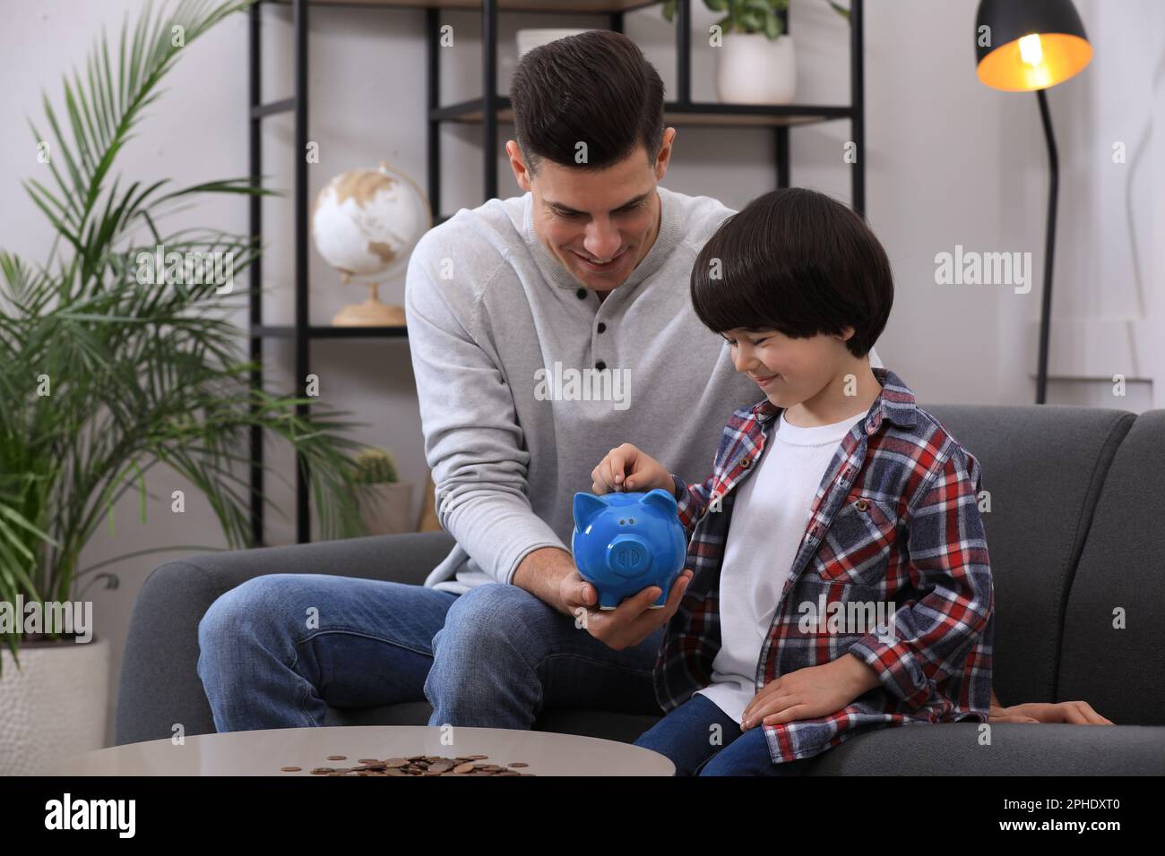Little boy with his father putting coin into piggy bank at home Stock ...