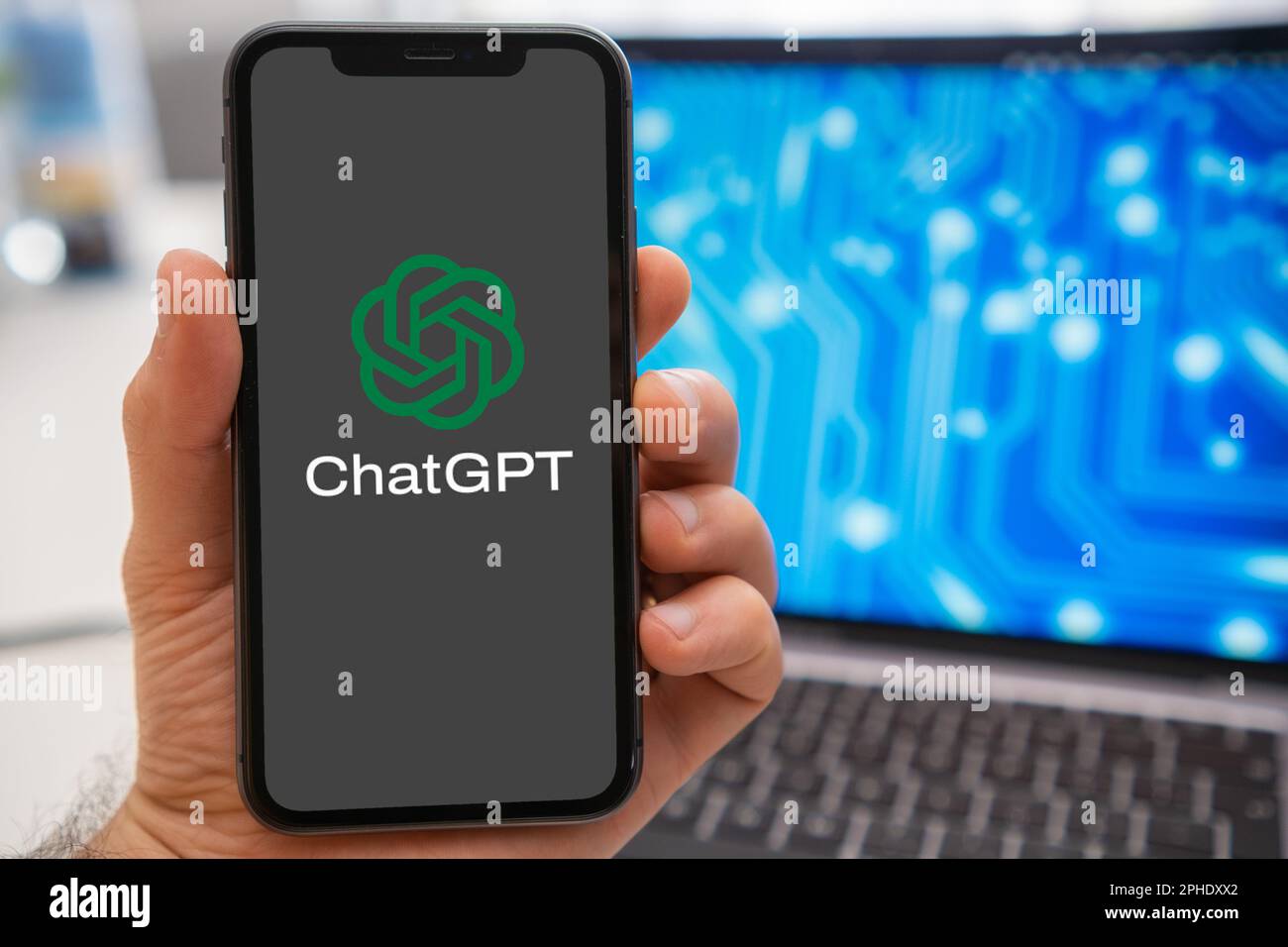 ChatGPT logo of neural network on the screen of smartphone in mans hand and laptop with neuronet on the splash screen on the background. Artificial intelligence concept. March 2023, Prague, Czech Republic  Stock Photo