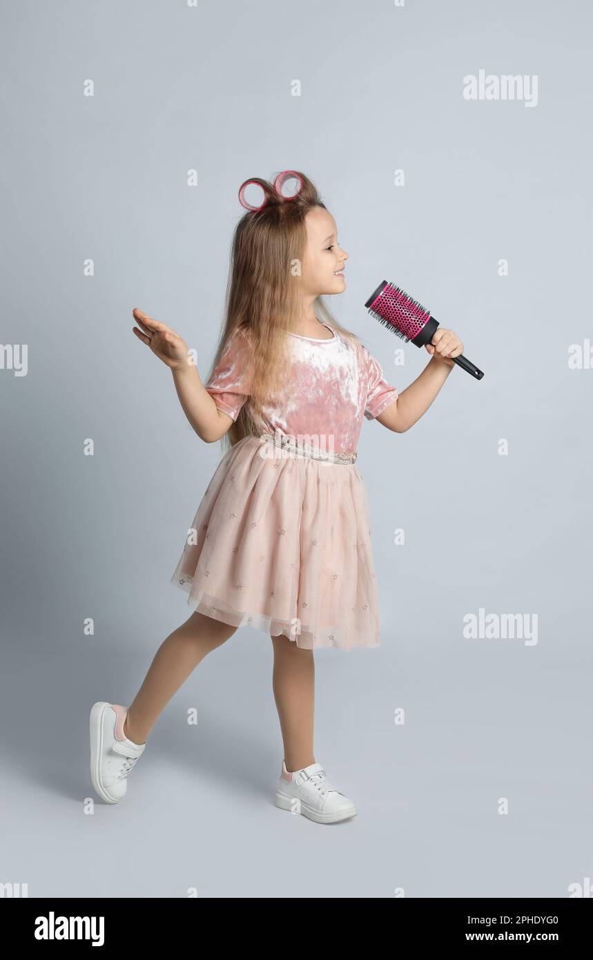 Cute little girl with hairbrush singing on light grey background Stock