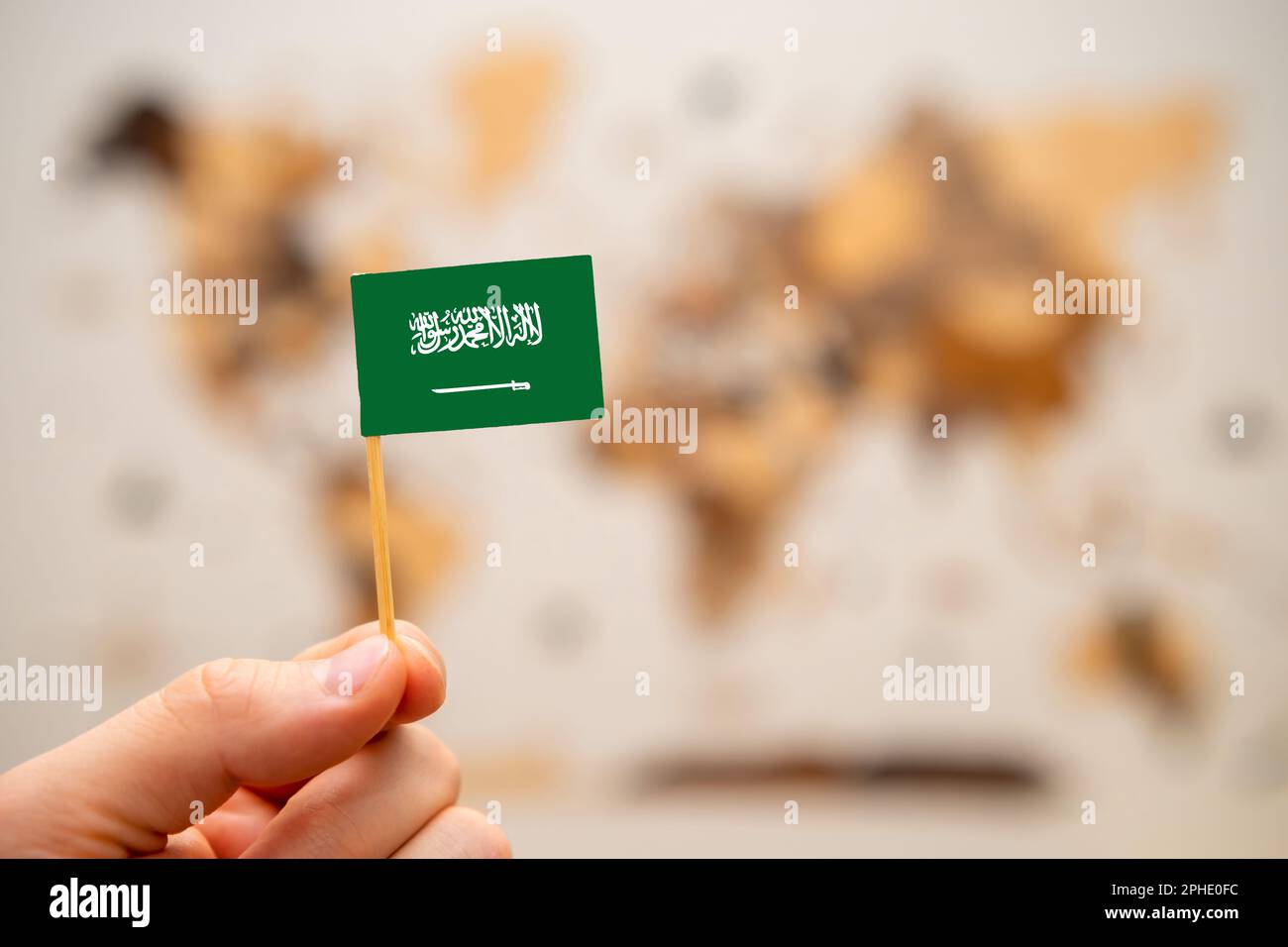 Saudi Arabia flag in mans hand on the wooden world map background. Global economy and geopolitics concept.  Stock Photo