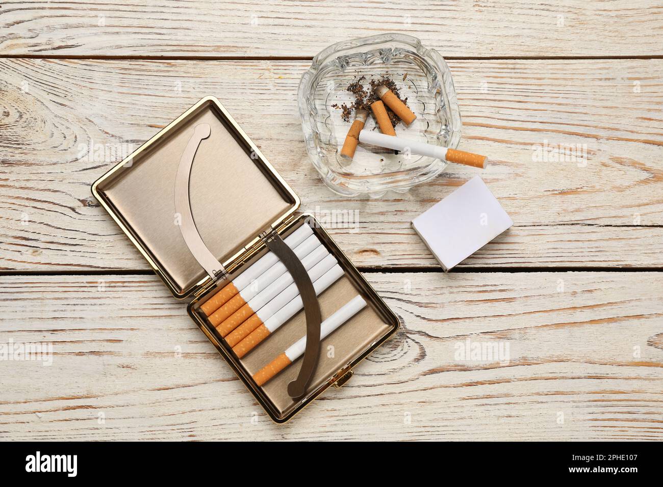 Cigarettes in case, matchbox and ashtray with stubs on white wooden table,  flat lay Stock Photo