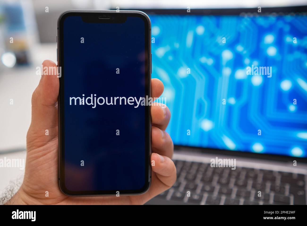Midjourney logo of neural network on the screen of smartphone in mans hand and laptop with neuronet on the splash screen on the background. Artificial intelligence concept, March 2023, Prague, Czech Republic. Stock Photo