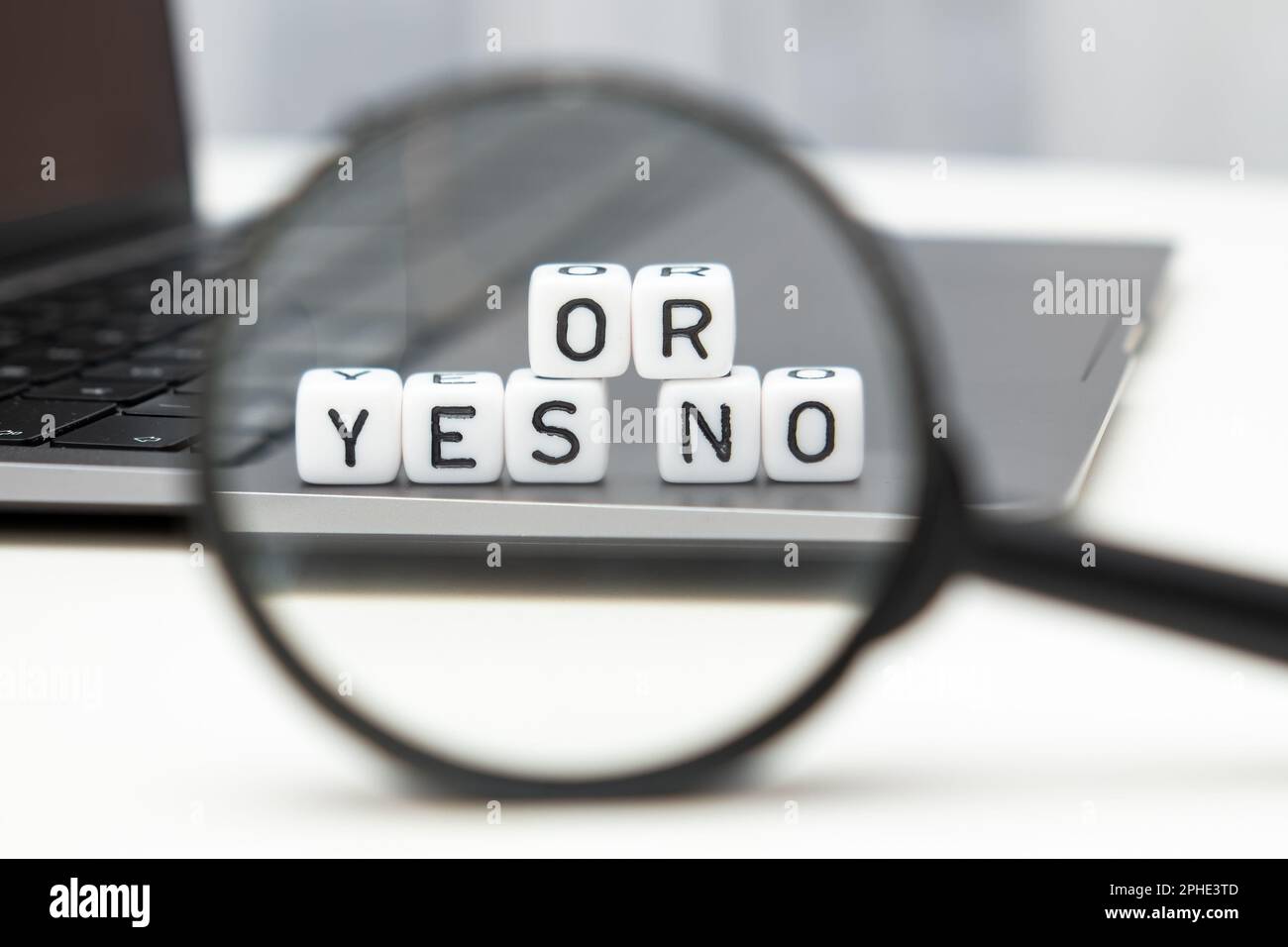 Yes or no on cubes through a magnifying glass and laptop on the background. Chose or shopping concept.  Stock Photo
