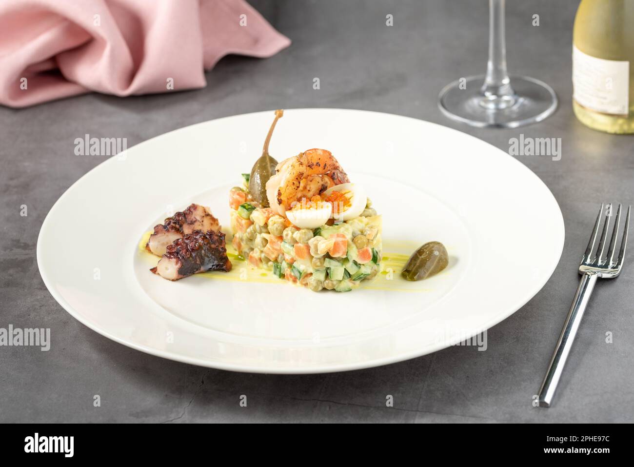 Russian salad with aioli sauce, shrimp, octopus and capers on a white porcelain plate Stock Photo