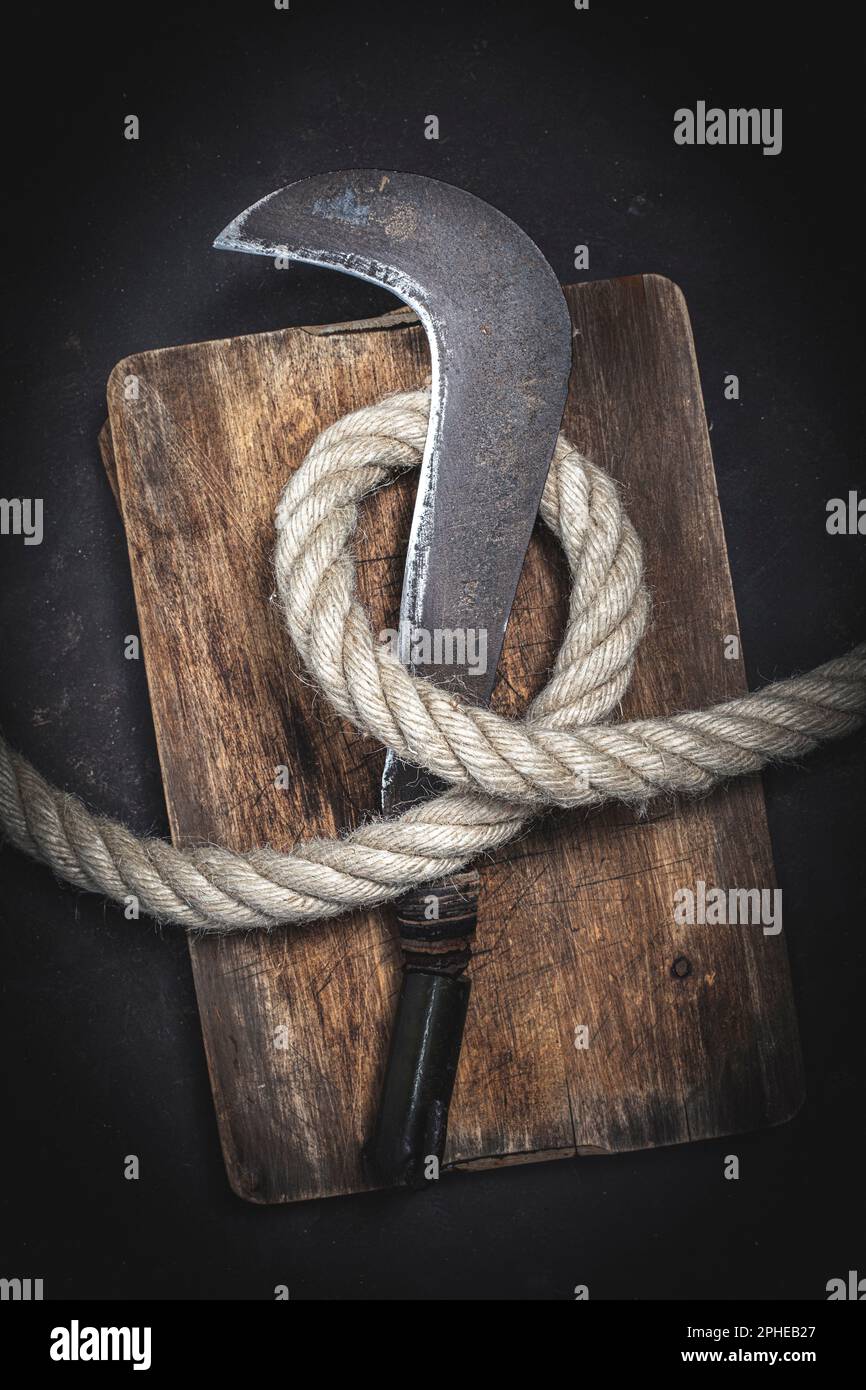 old billhook wrapped with thick rope on a wooden background Stock Photo