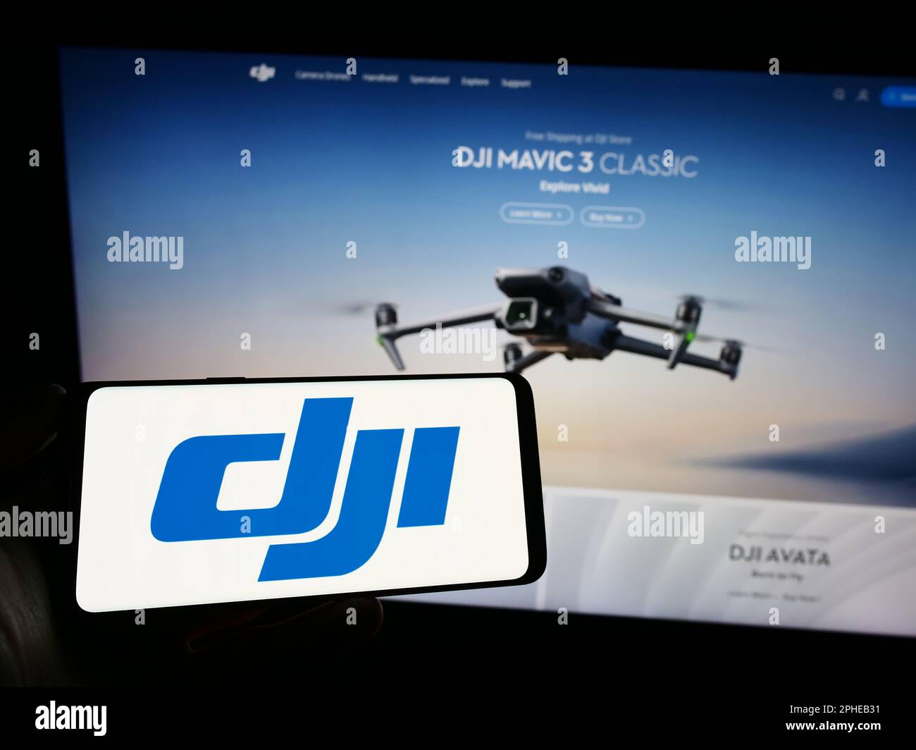 Person holding mobile phone with logo of drone company SZ DJI Technology Co. Ltd. on screen in front of business web page. Focus on phone display. Stock Photo