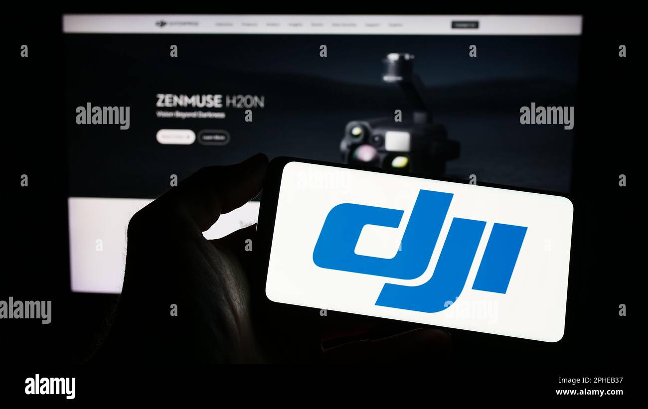 Person holding cellphone with logo of drone company SZ DJI Technology Co. Ltd. on screen in front of business webpage. Focus on phone display. Stock Photo