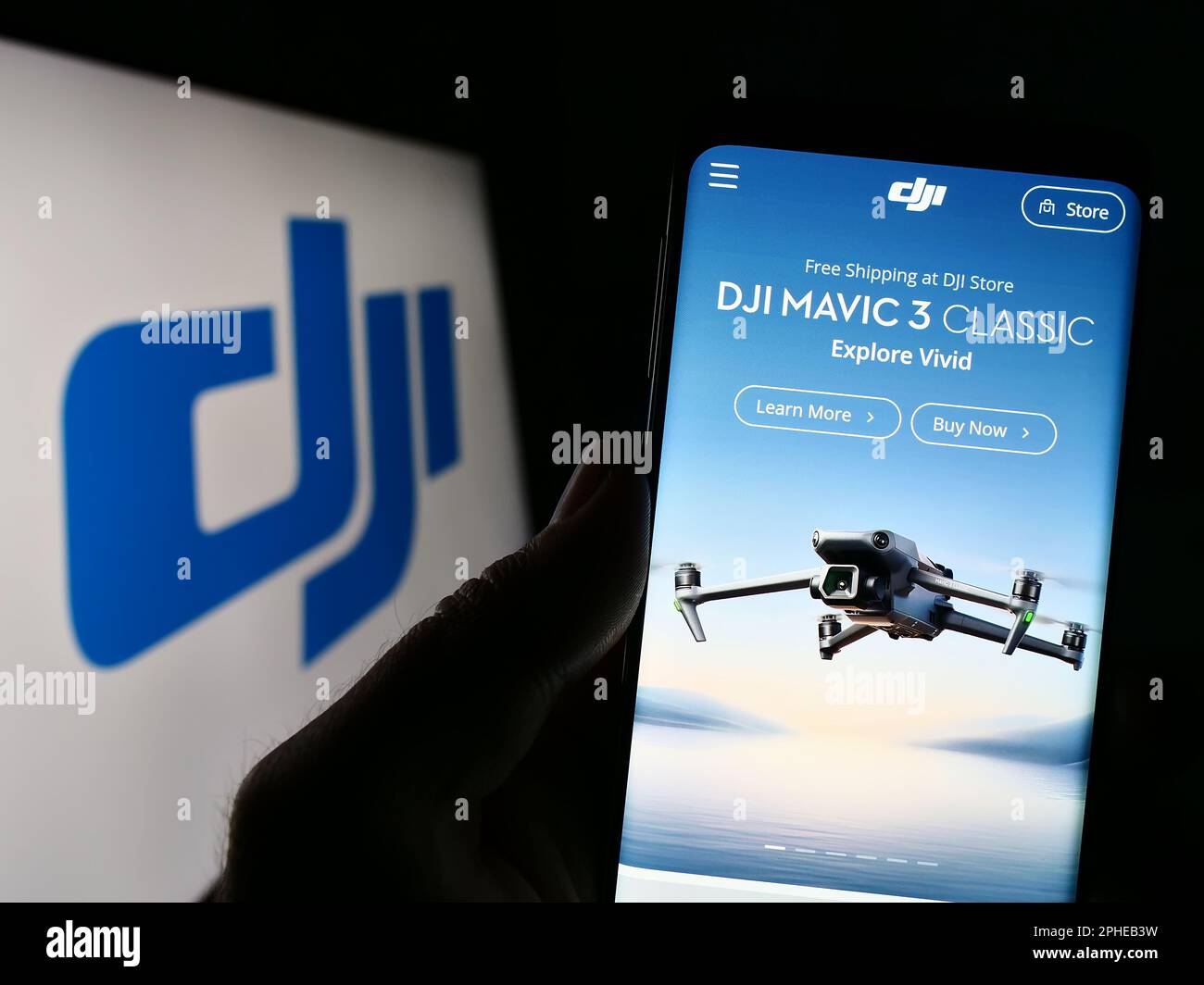 Person holding cellphone with website of drone company SZ DJI Technology Co. Ltd. on screen in front of logo. Focus on center of phone display. Stock Photo