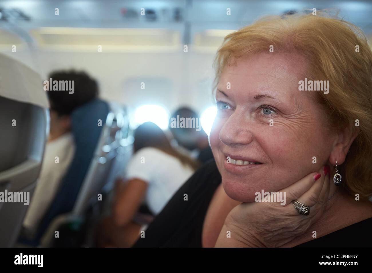 Portrait of senior woman with dreamy look while traveling by airplane. Passengers in airplane cabin during flight. Stock Photo