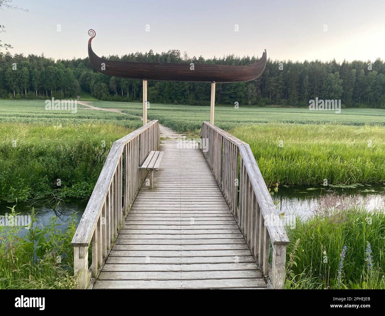 A beautiful wooden bridge with a boat figure leading across a lush marshy landscape in Stockholm Stock Photo