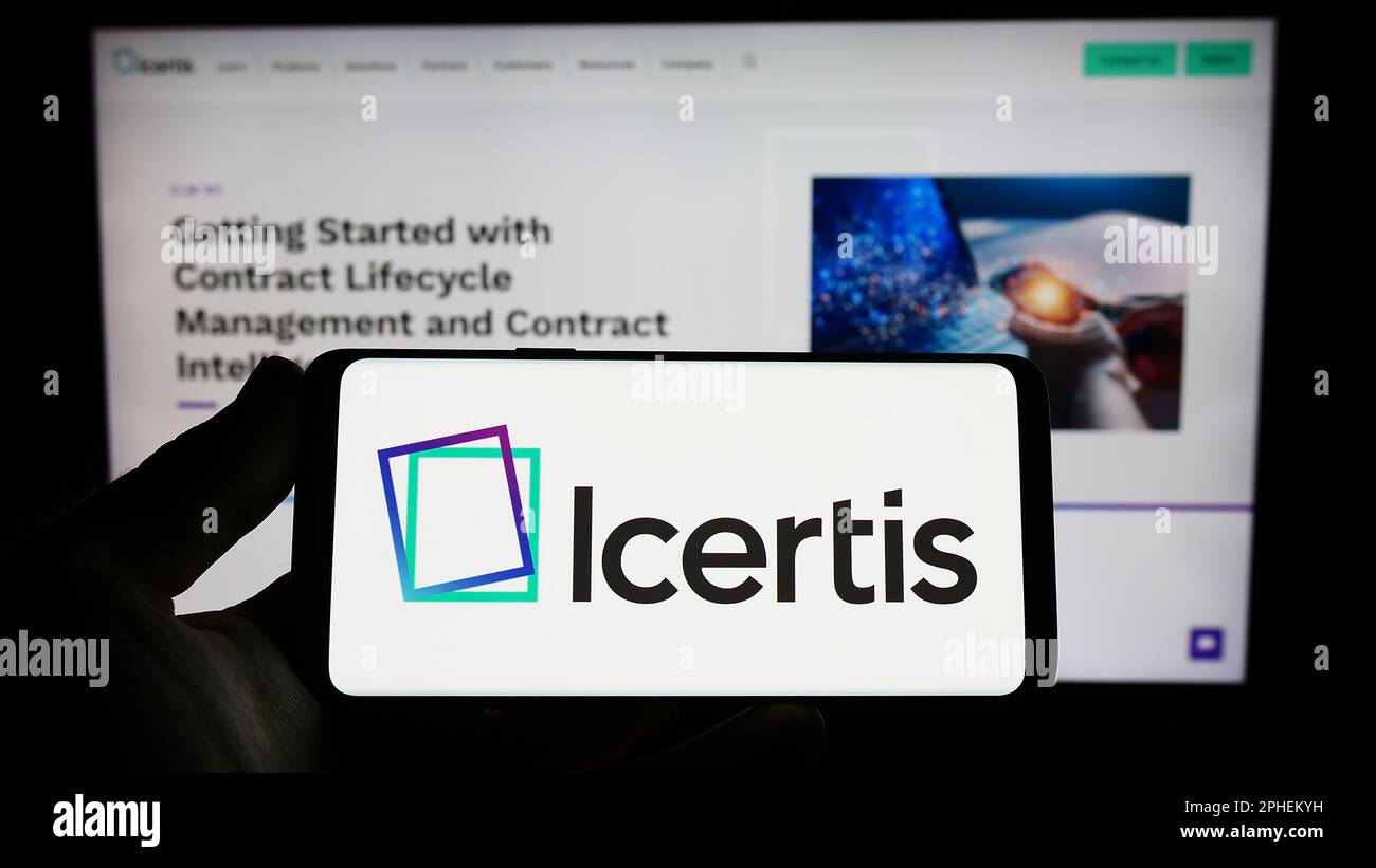 Person holding smartphone with logo of US CLM software company Icertis Inc. on screen in front of website. Focus on phone display. Stock Photo
