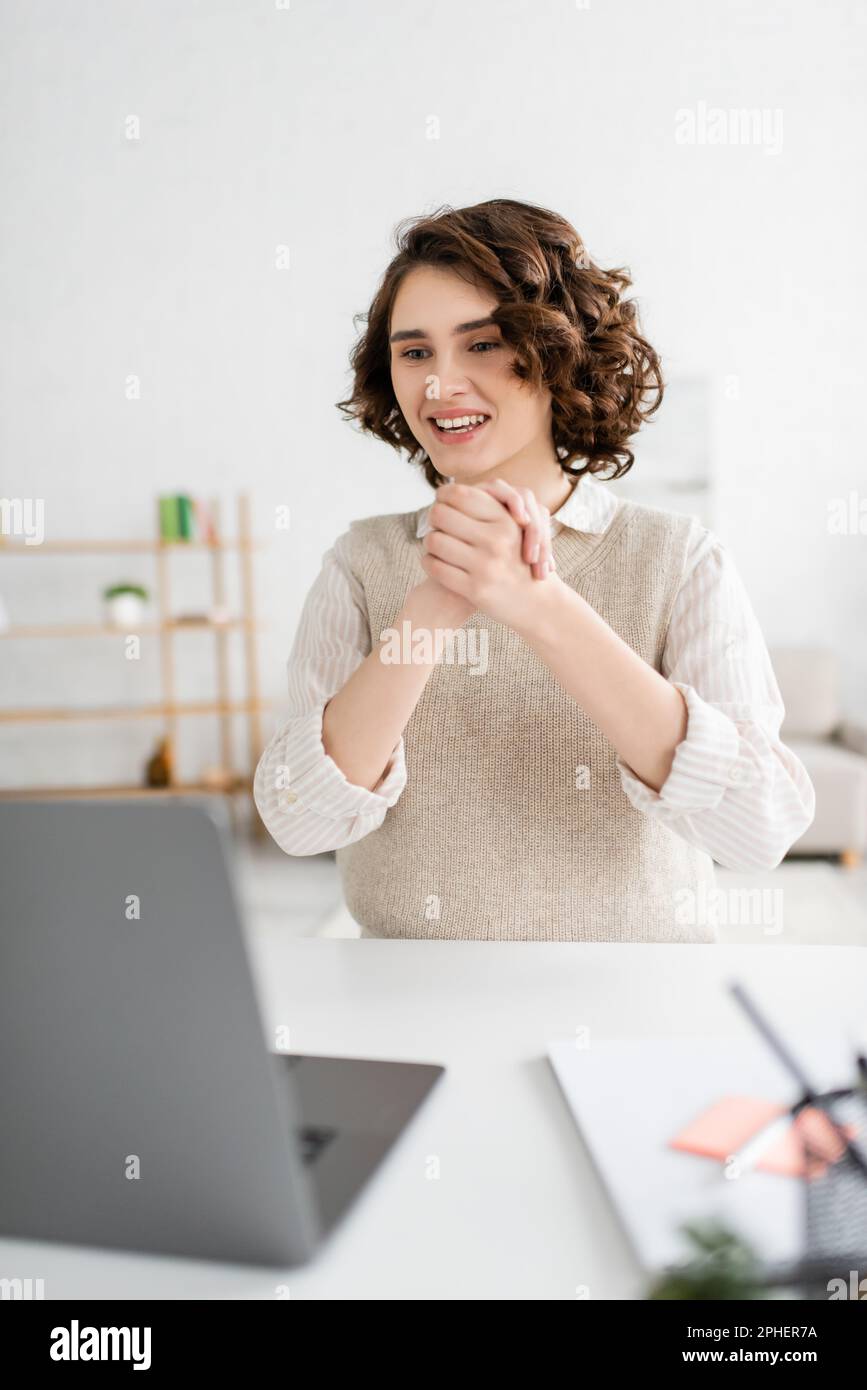 cheerful woman showing clenched hands while teaching sign language during online lesson on laptop,stock image Stock Photo