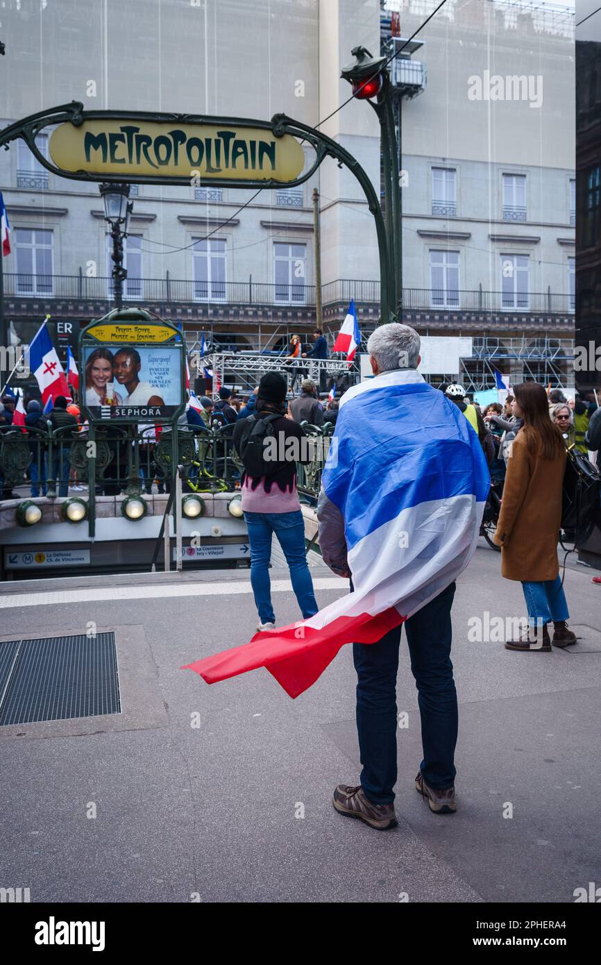 Paris, France. March 25, 2023. A man wearing a French flag in front of a metro entrance in a Protest against the pension reform outside the Palais-Roy Stock Photo