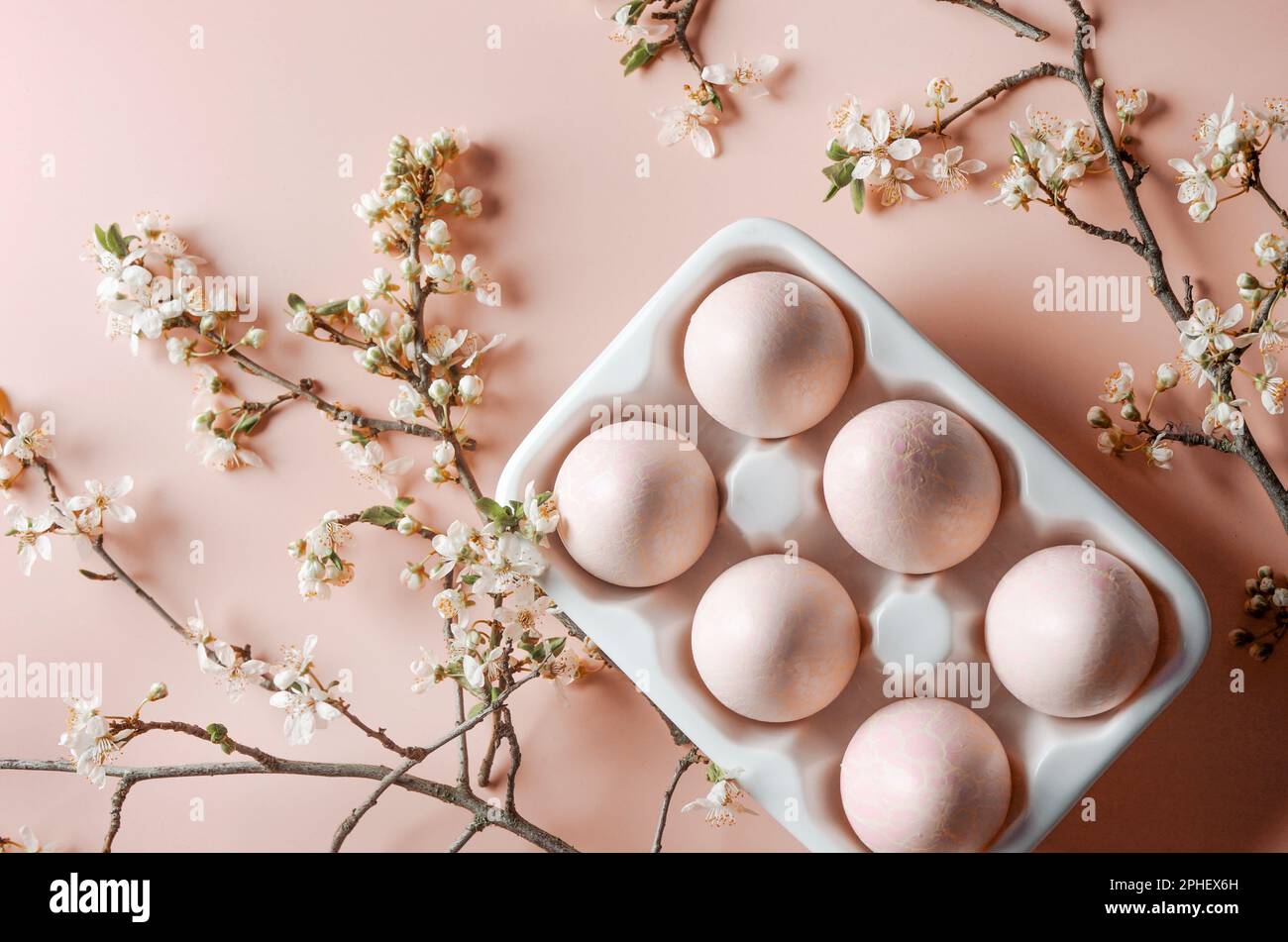 Easter eggs in holder with cherry blossom branches at pale pink background, top view Stock Photo