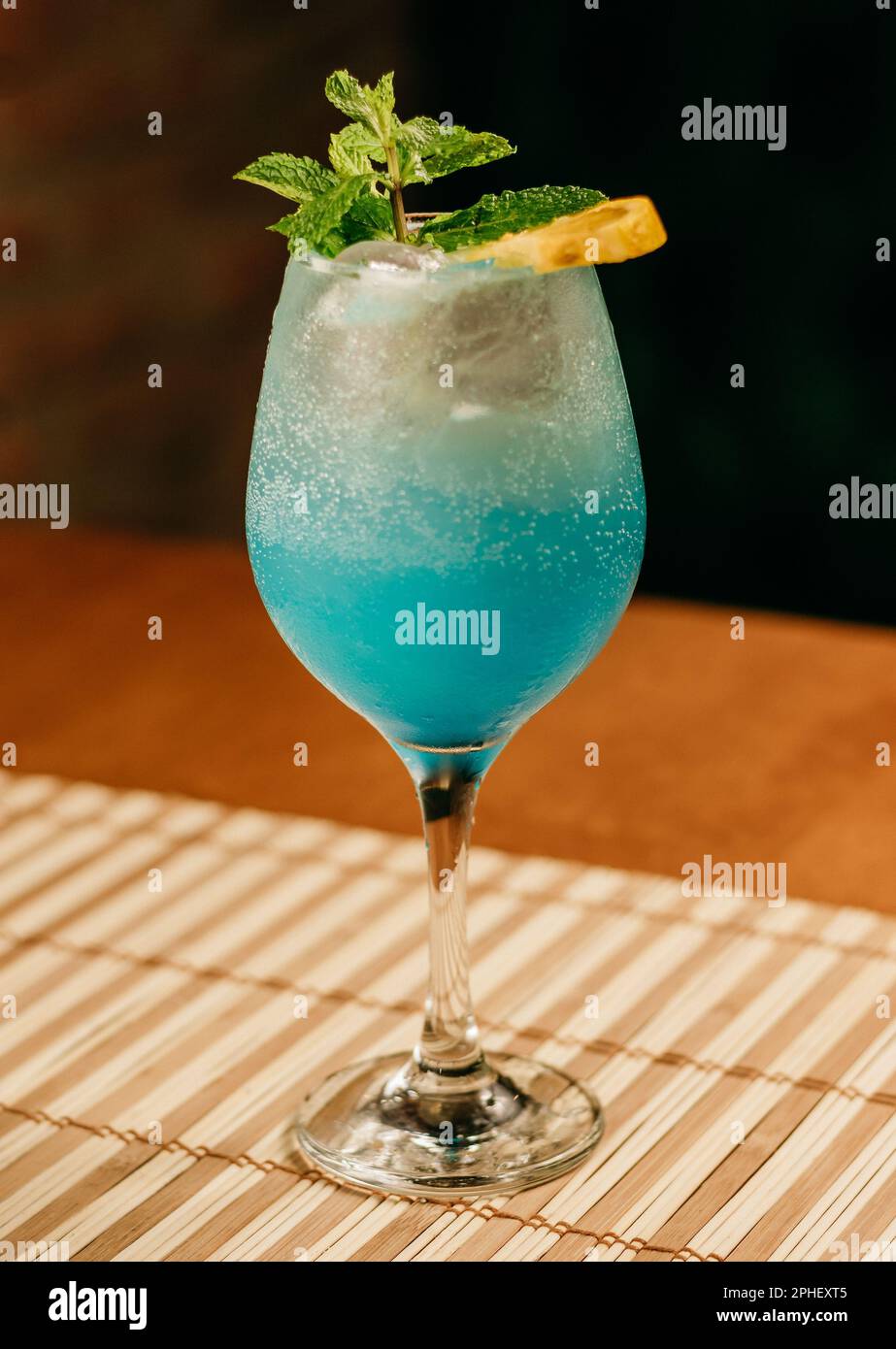 A close-up image of a vibrant blue cocktail with ice in a tall glass ...