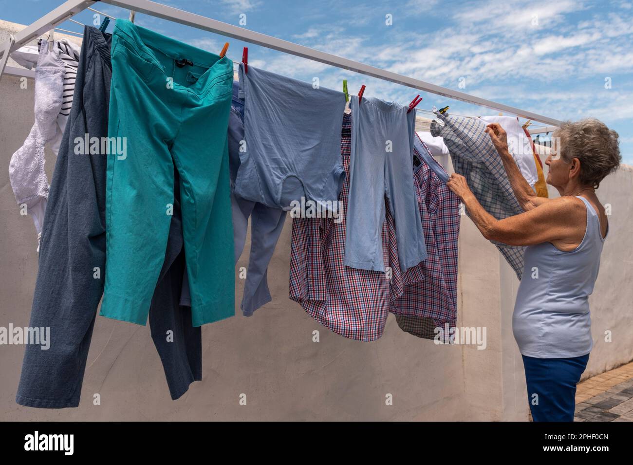 Langebaan, South Africa. 2023. Elderly woman hanging out the washing on a windy day in her backyard. Stock Photo