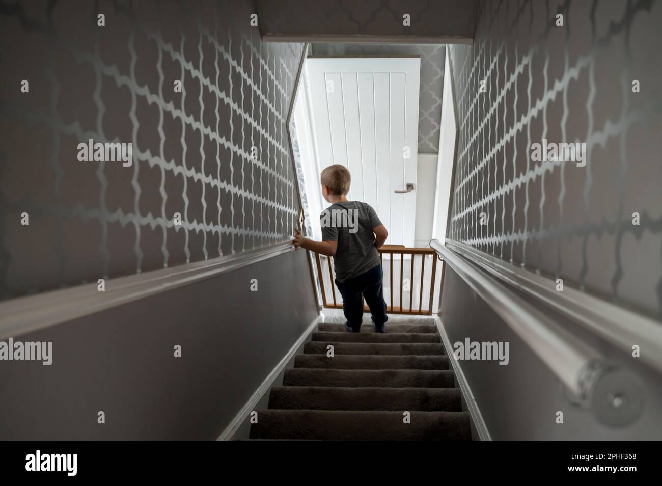Child going down the steep stairs at home with baby safety gate. Boy in