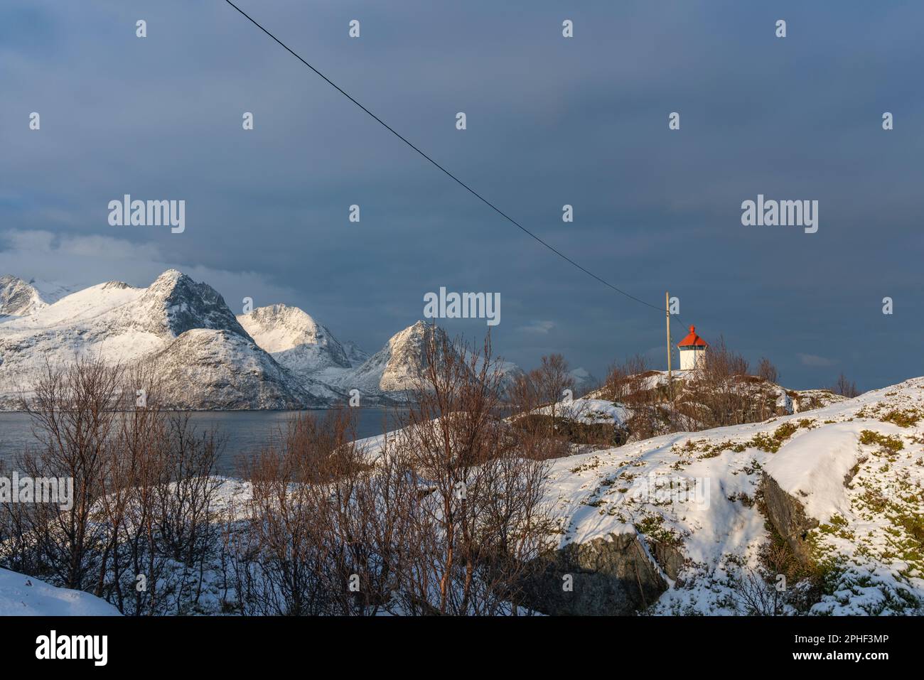 Panorama mit Leuchtturm im Øyfjorden und den schneebedeckten Bergen von Senja, genannt Kongan und Skultran. rotes Leuchtfeuer auf der Insel Husøy Stock Photo