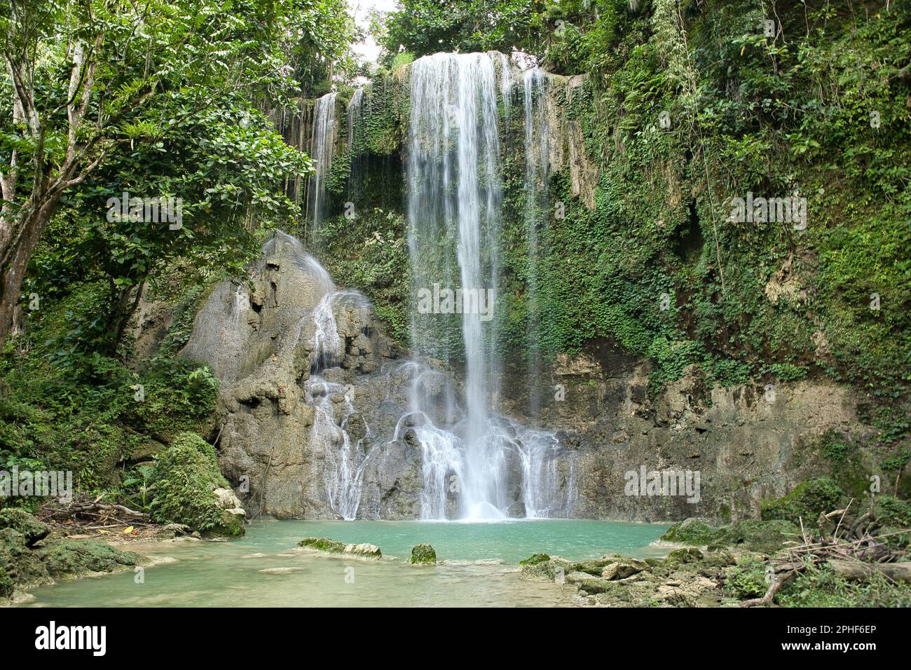 The idyllic Kawasan Waterfall in Siquijor in the Philippines that flow into a natural pool of water surrounded by the light-lit rainforest. Stock Photo