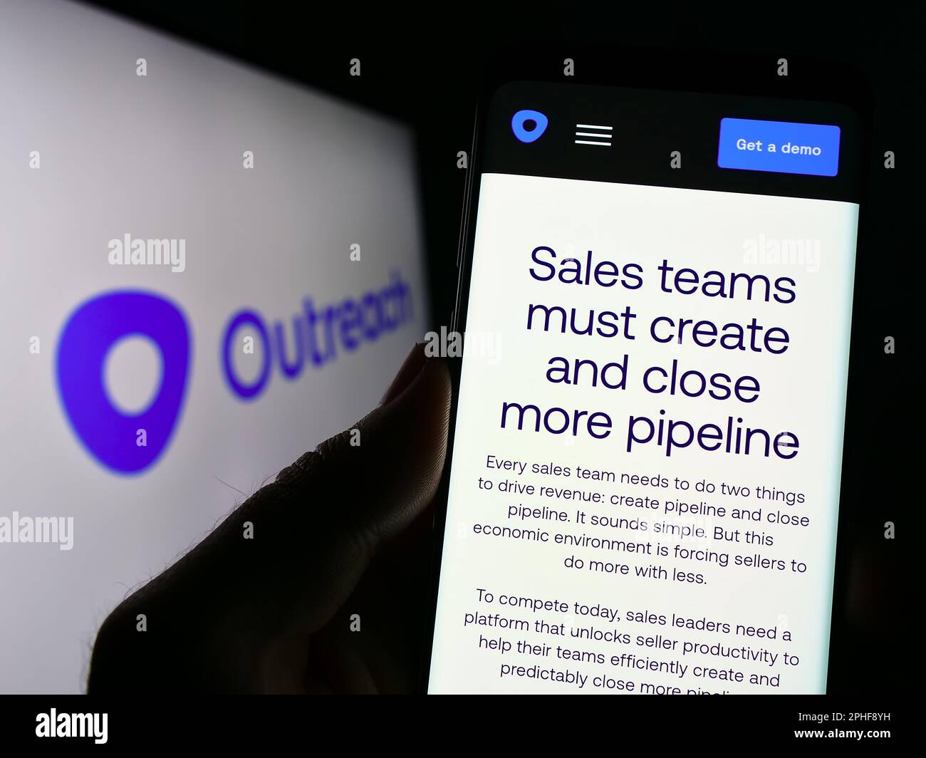Person holding smartphone with webpage of US sales software company Outreach.io on screen in front of logo. Focus on center of phone display. Stock Photo