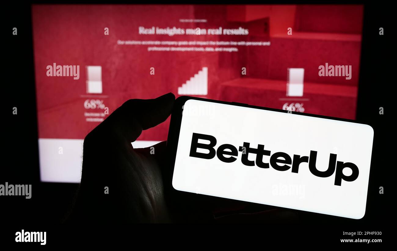 Person holding cellphone with logo of US coaching company BetterUp on screen in front of business webpage. Focus on phone display. Stock Photo
