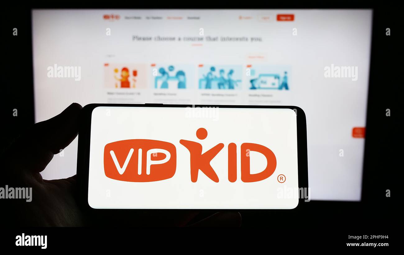 Person holding smartphone with logo of e-learning company VIPKid on screen in front of website. Focus on phone display. Stock Photo