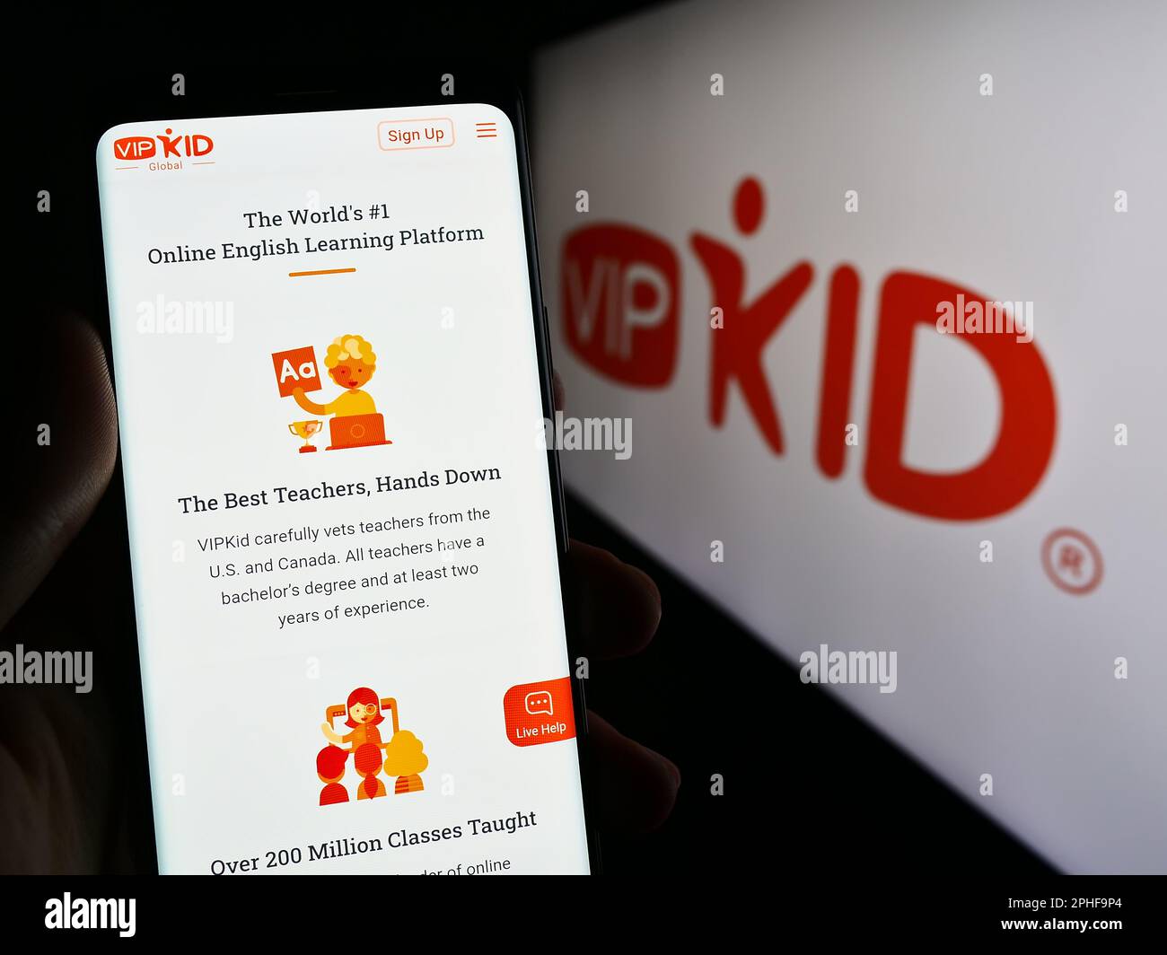 Person holding cellphone with website of e-learning company VIPKid on screen in front of business logo. Focus on center of phone display. Stock Photo