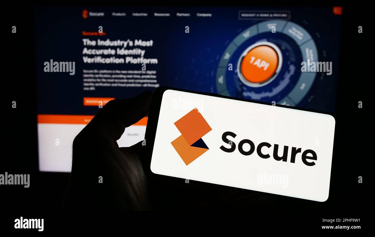 Person holding cellphone with logo of American identity verification company Socure Inc. on screen in front of webpage. Focus on phone display. Stock Photo