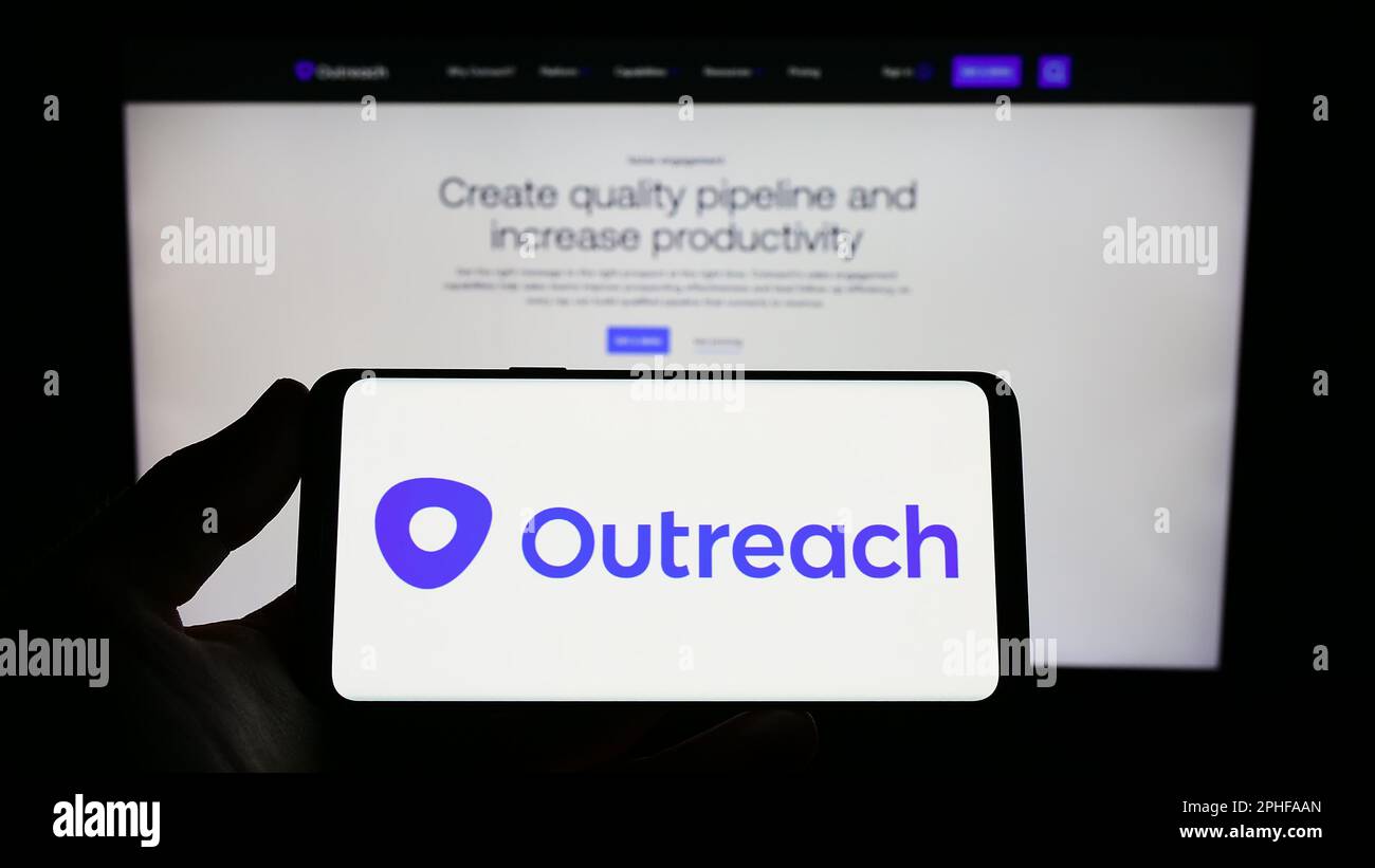 Person holding smartphone with logo of US sales software company Outreach.io on screen in front of website. Focus on phone display. Stock Photo