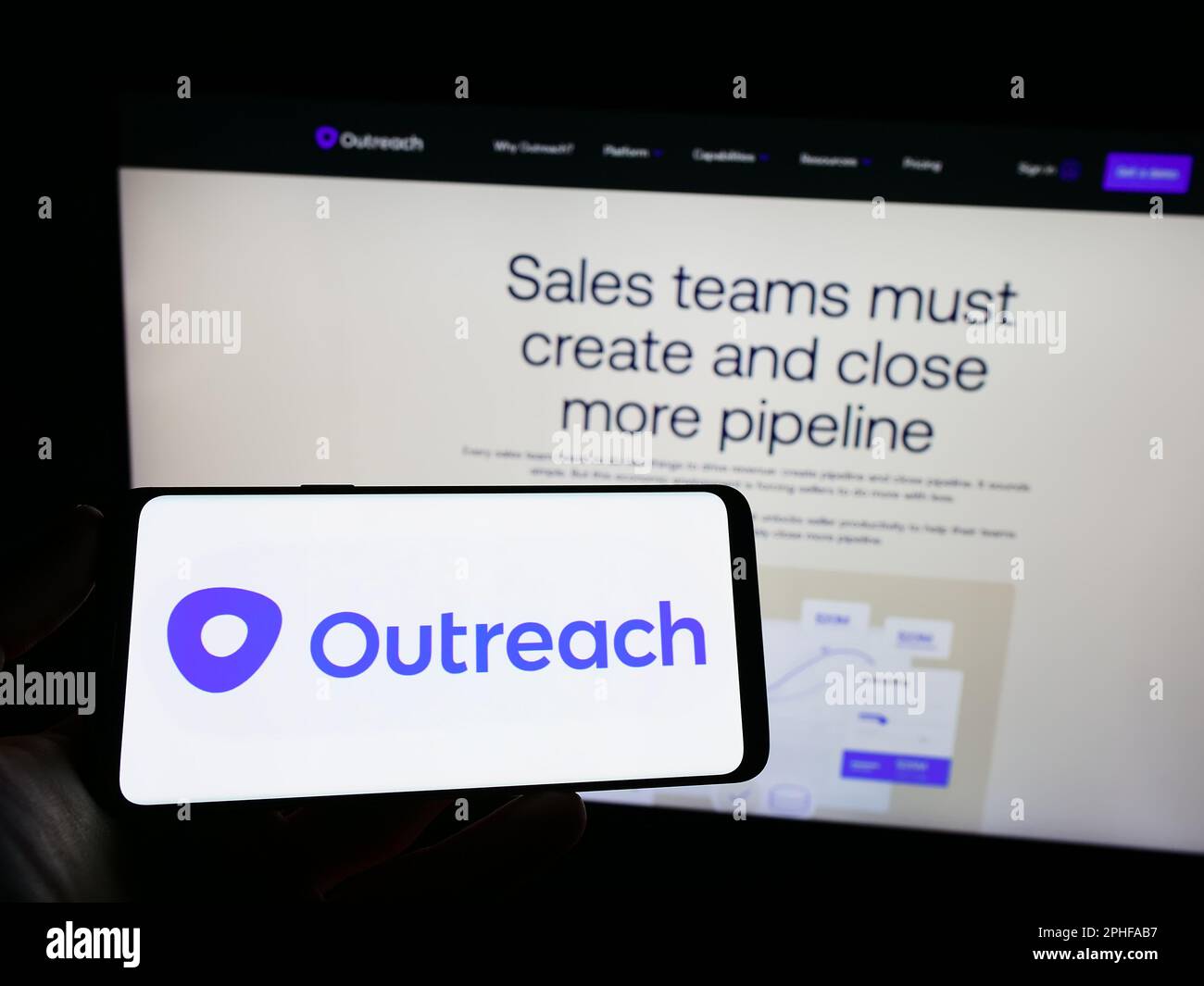 Person holding mobile phone with logo of American sales software company Outreach.io on screen in front of web page. Focus on phone display. Stock Photo