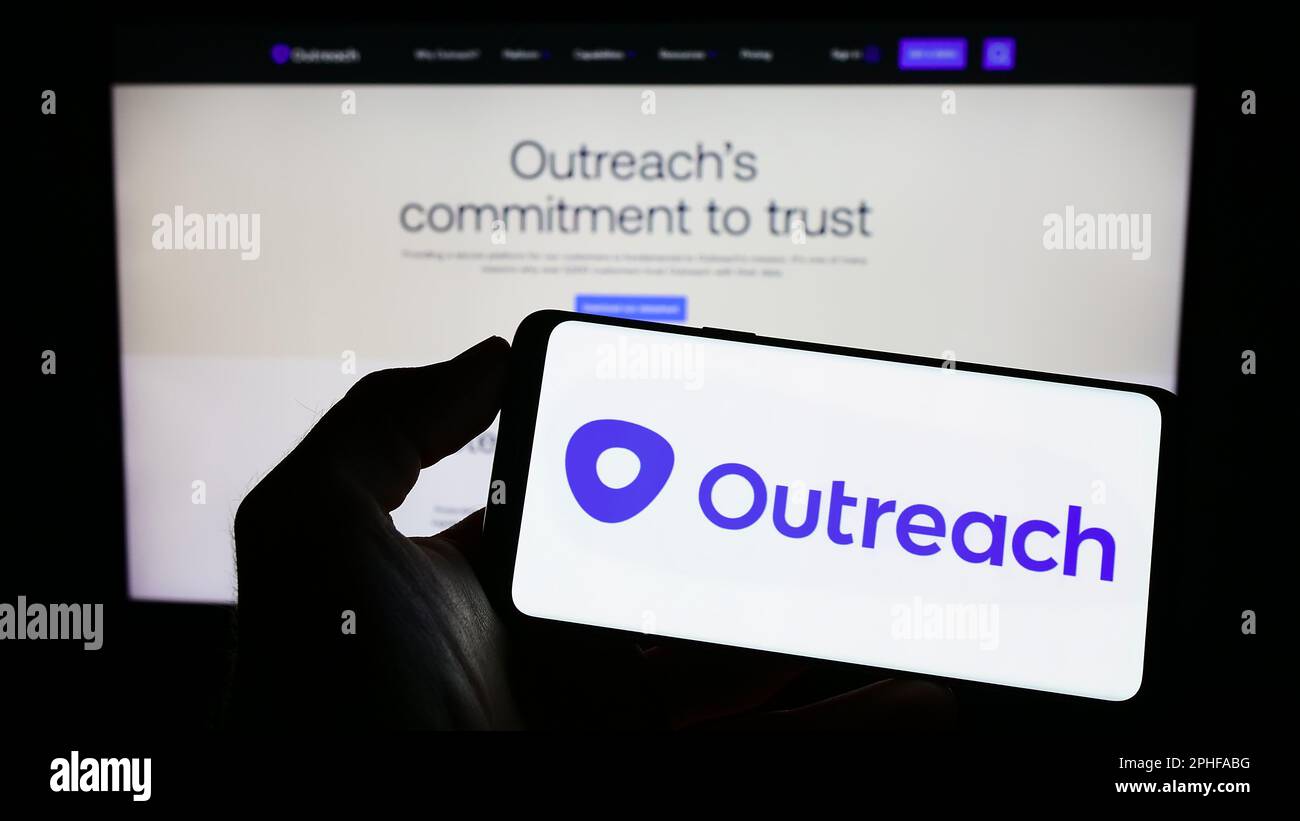 Person holding cellphone with logo of US sales software company Outreach.io on screen in front of business webpage. Focus on phone display. Stock Photo