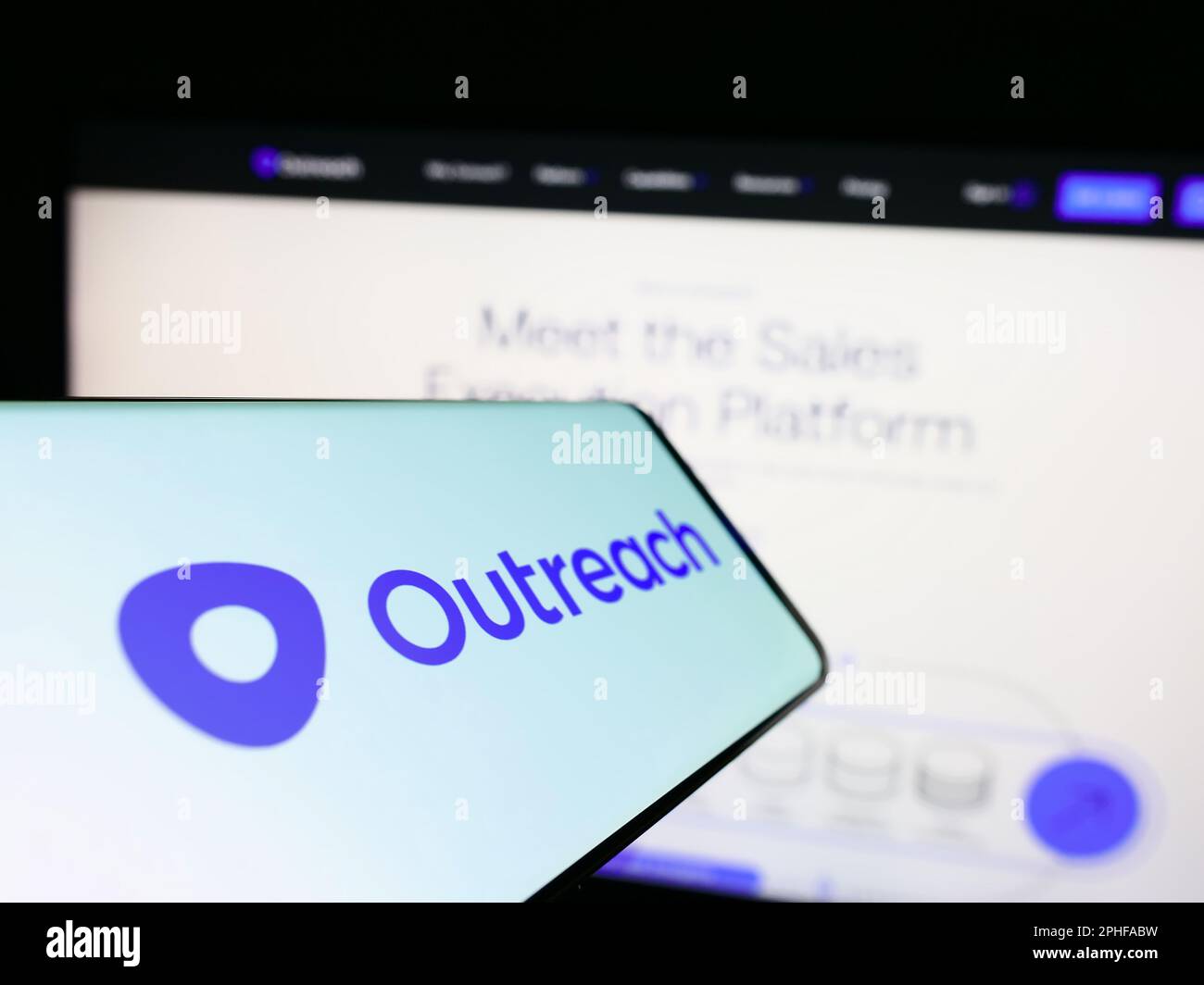 Mobile phone with logo of American sales software company Outreach.io on screen in front of business website. Focus on center of phone display. Stock Photo