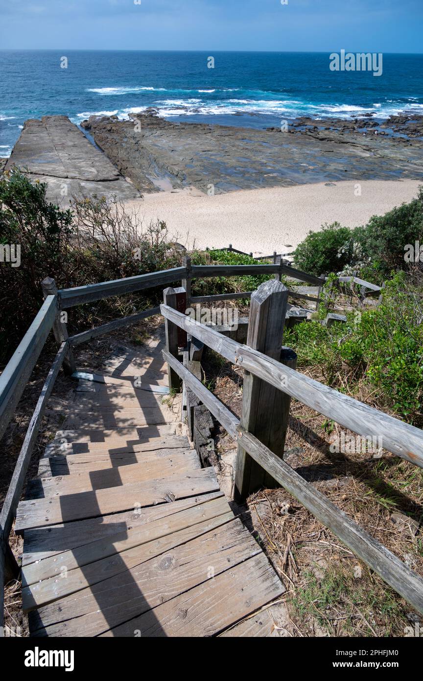 Wooden steps lead down the cliff path beneath Norah Head lighthouse to the beach below on The Pacific Coast, New South Wales, NSW, Australia. Stock Photo