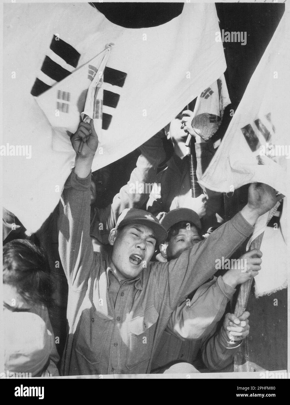 This anti-Communist North Korean just released from a prisoner of war camp is serving as a kind of cheerleader for fellow ex Prisoners of War as they shout their joy of reaching Seoul. The flags are of the Republic of South Korea, Circa 1954. (Photo by United States Information agency) Stock Photo