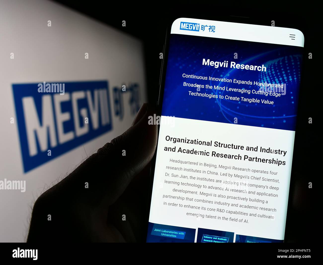 Person holding cellphone with webpage of Chinese company Megvii Technology Limited on screen in front of logo. Focus on center of phone display. Stock Photo