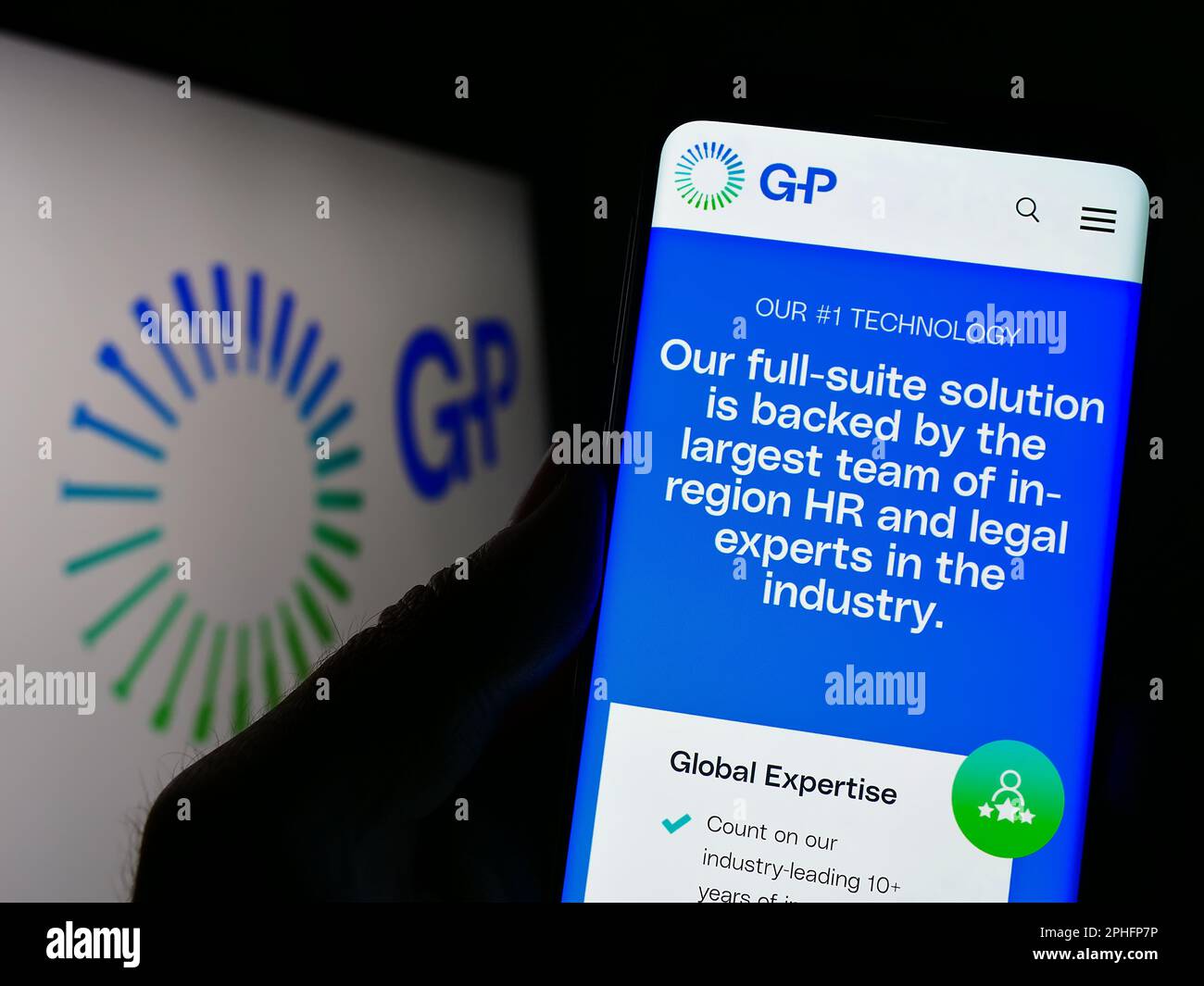 Person holding cellphone with webpage of company Globalization Partners LLC (GP) on screen in front of logo. Focus on center of phone display. Stock Photo