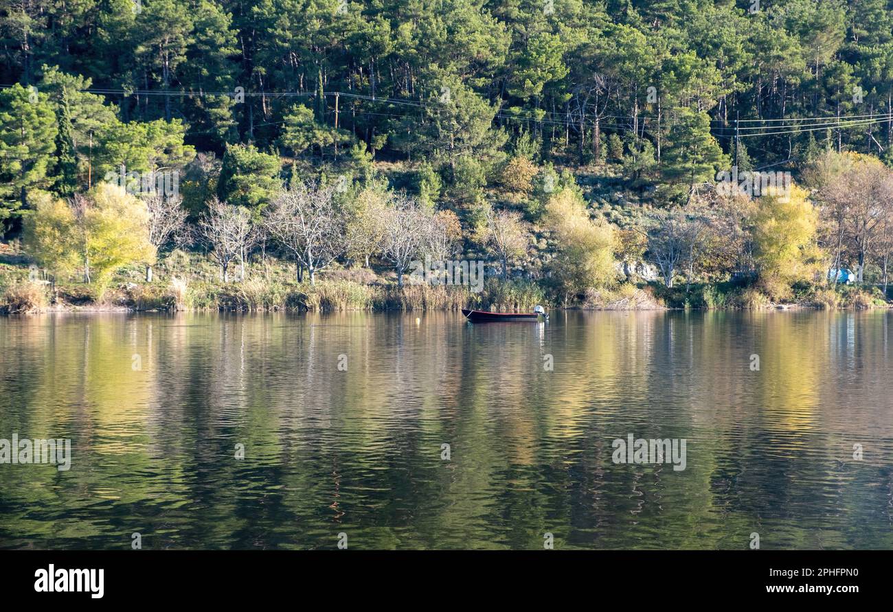Ioannina city Pamvotis Lake, Epirus Greece. Destination Giannena lakefront forest background, moored boat, tree reflects on colorful water. Stock Photo
