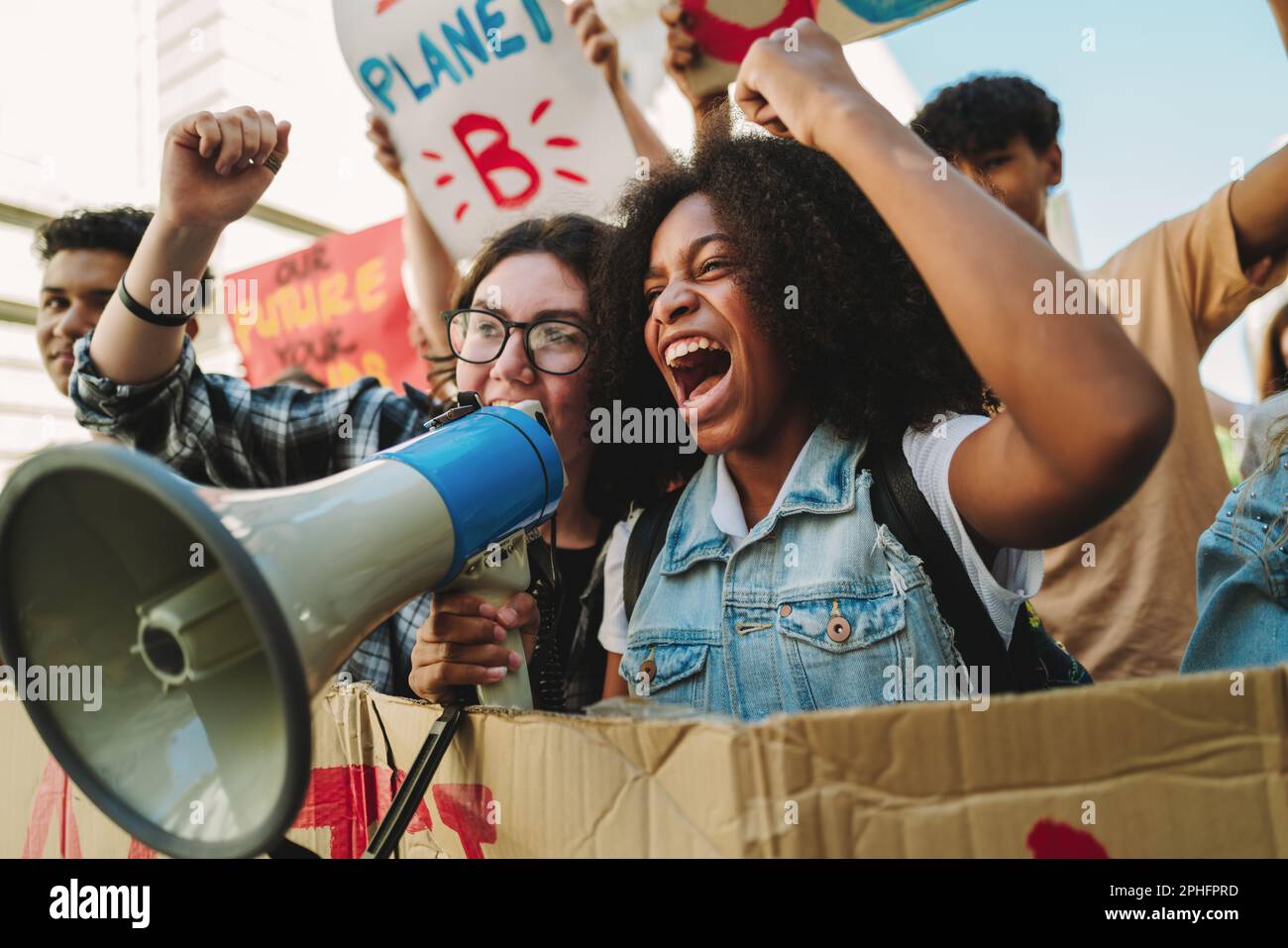 Youth climate activists shouting on a megaphone while marching against climate change. Young people protesting against global warming and pollution. T Stock Photo