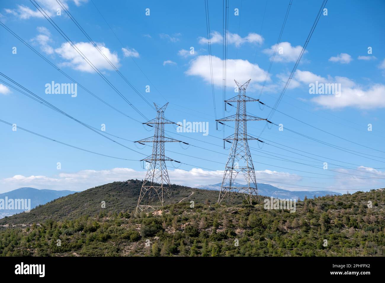 High voltage power lines and pylons on mountain, blue sky background ...