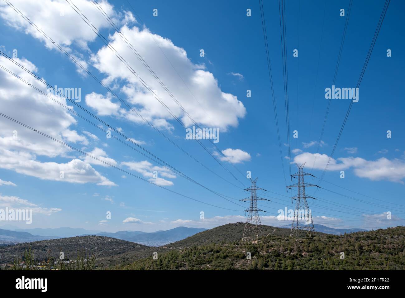 High voltage power lines and pylons on mountain, blue sky background ...
