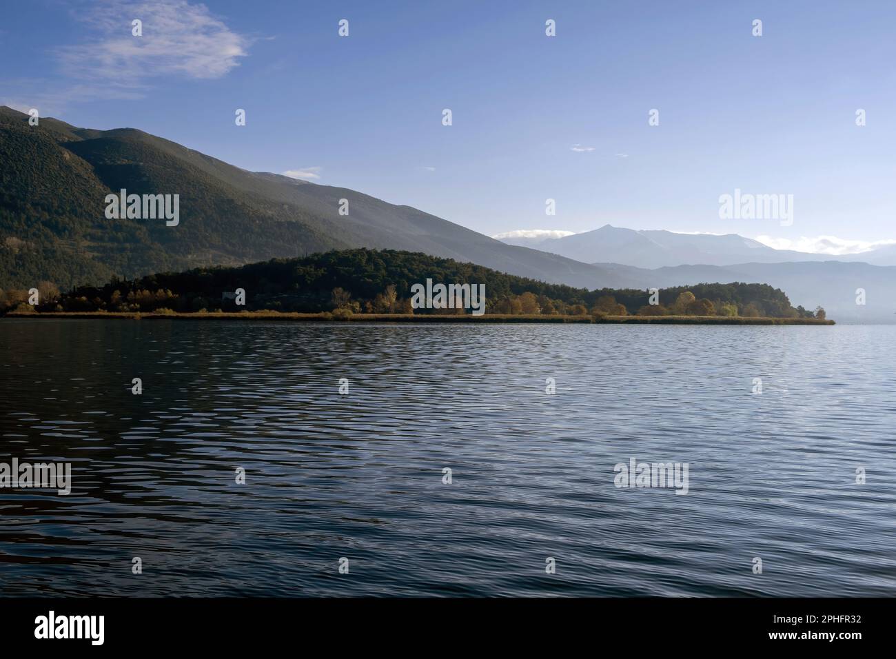 Greece, Pamvotis Lake, Ioannina city, Epirus. Destination Giannena, view of dark calm water, nisaki, nature, afternoon blue sky background. Stock Photo