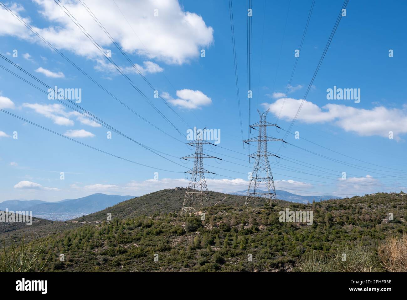 High voltage power lines and pylons on mountain, blue sky background ...