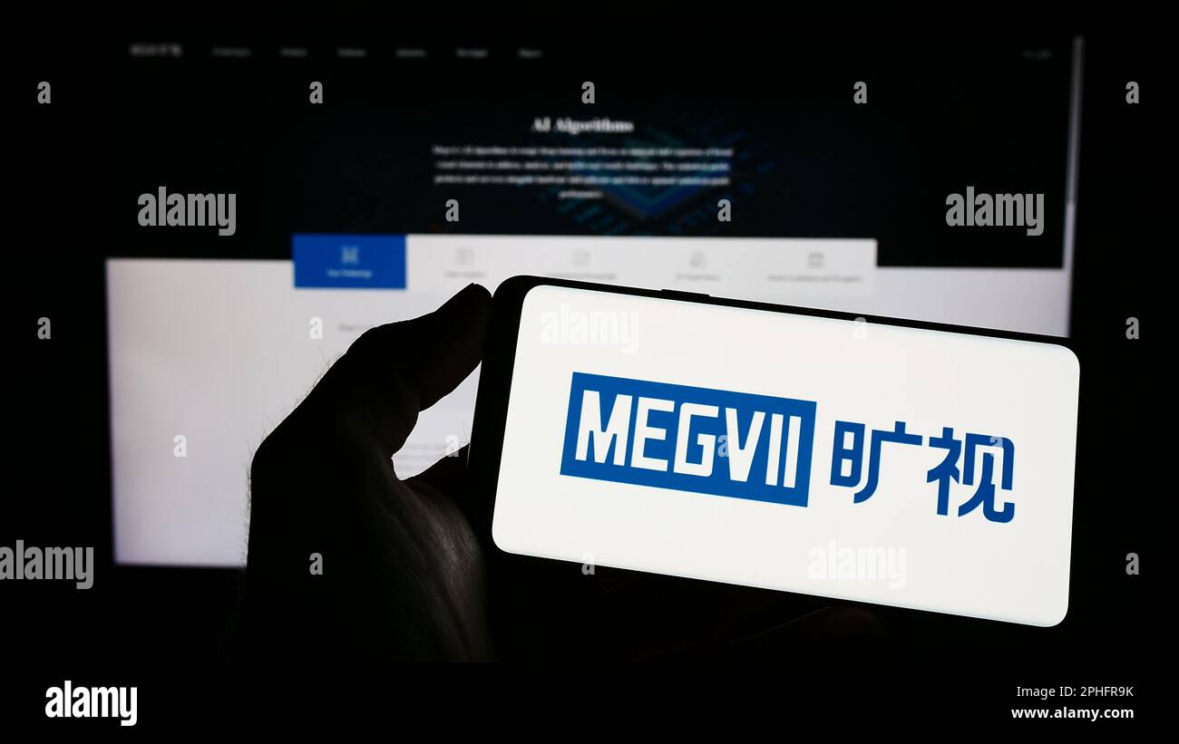 Person holding mobile phone with logo of Chinese company Megvii Technology Limited on screen in front of web page. Focus on phone display. Stock Photo