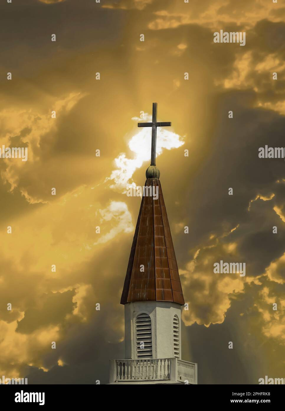 Church steeple with cross on top aganist a light streaked dramatic sky Stock Photo