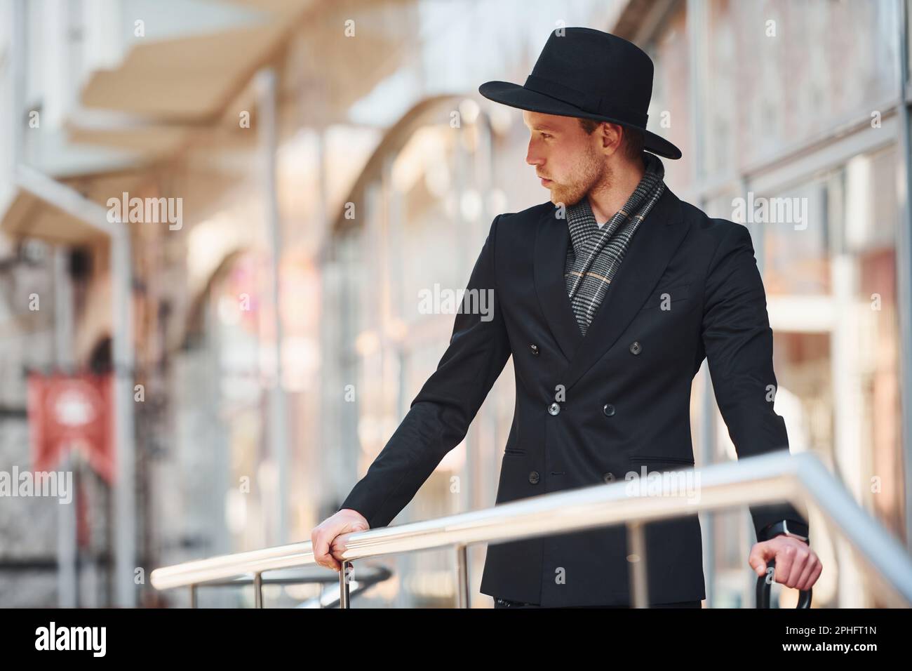 Elegant young man in black hat and with umbrella outdoors in the city