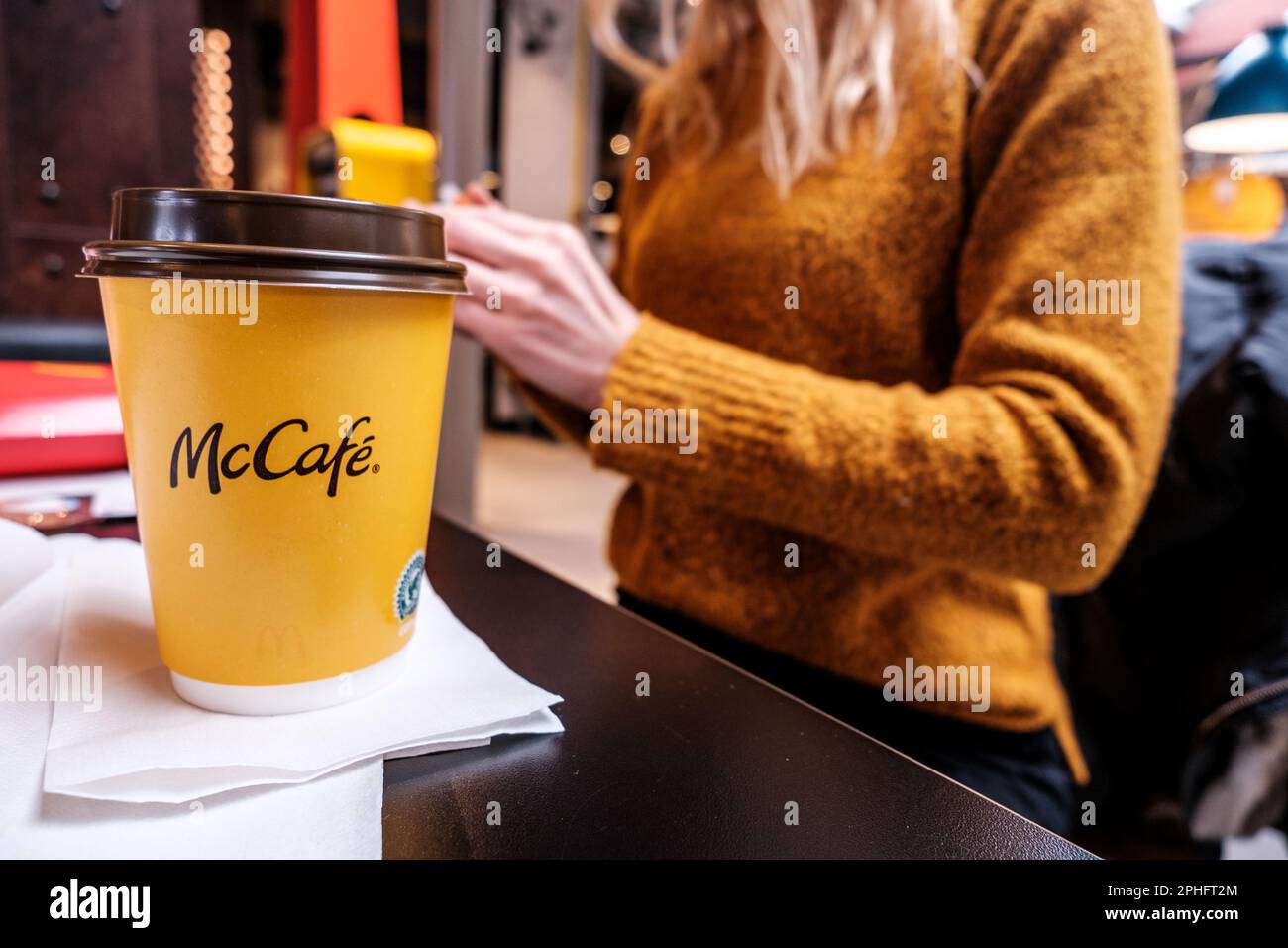 Sandnes, Norway, March 11 2023, Annonymous Woman Sitting Inside A  McDonalds Restaurant With A Take Away Paper Cup Of Coffee Beverage Stock Photo
